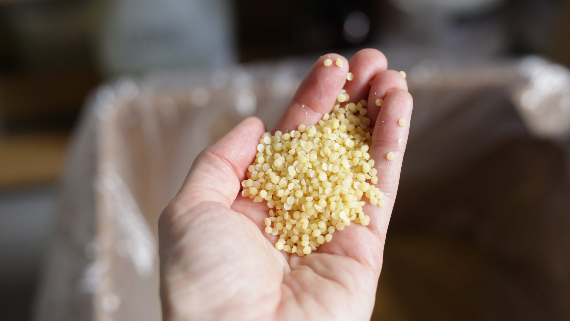 Hand holding raw beeswax pellets during candle making