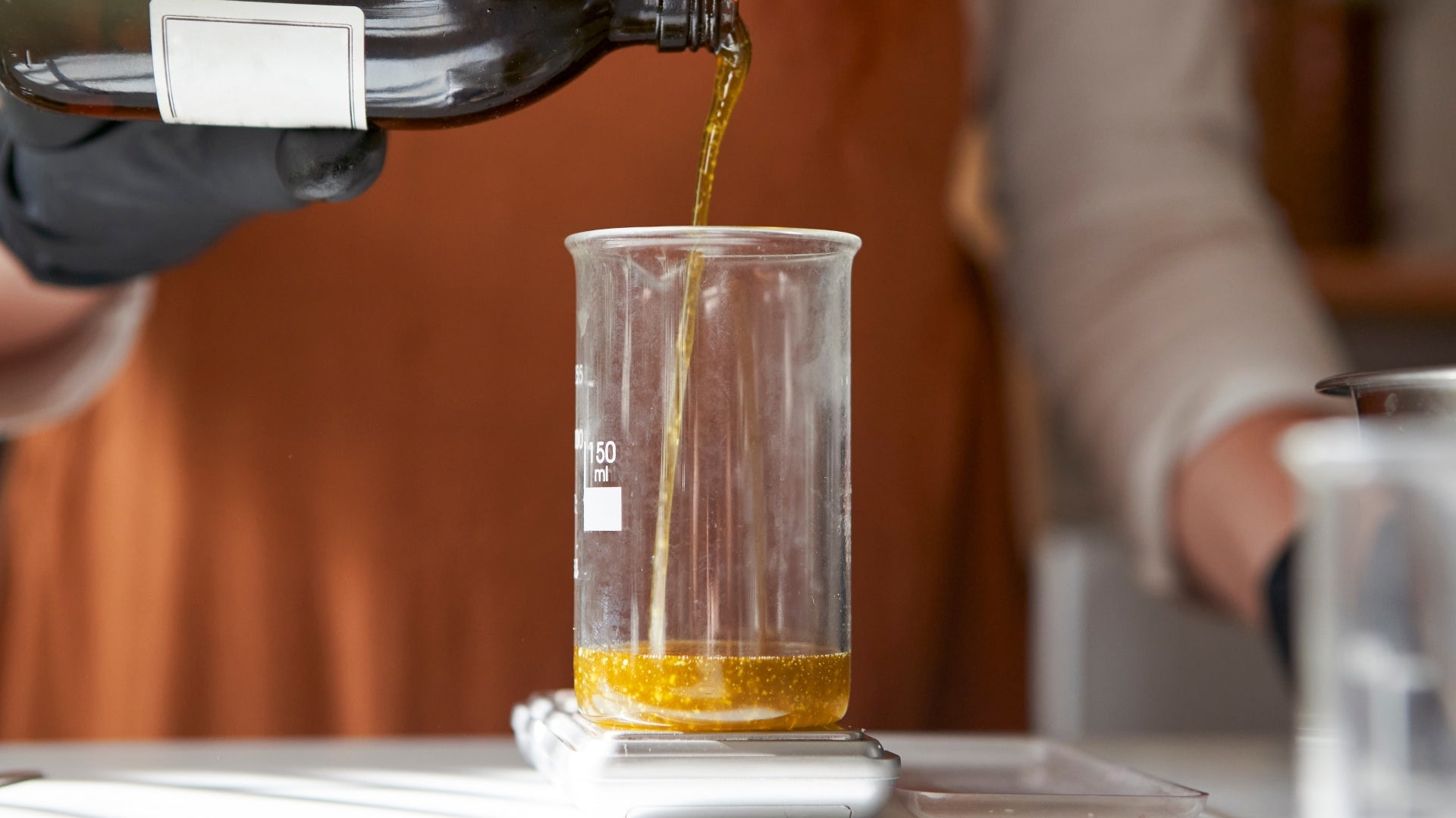 Pouring golden essential oil into a glass beaker